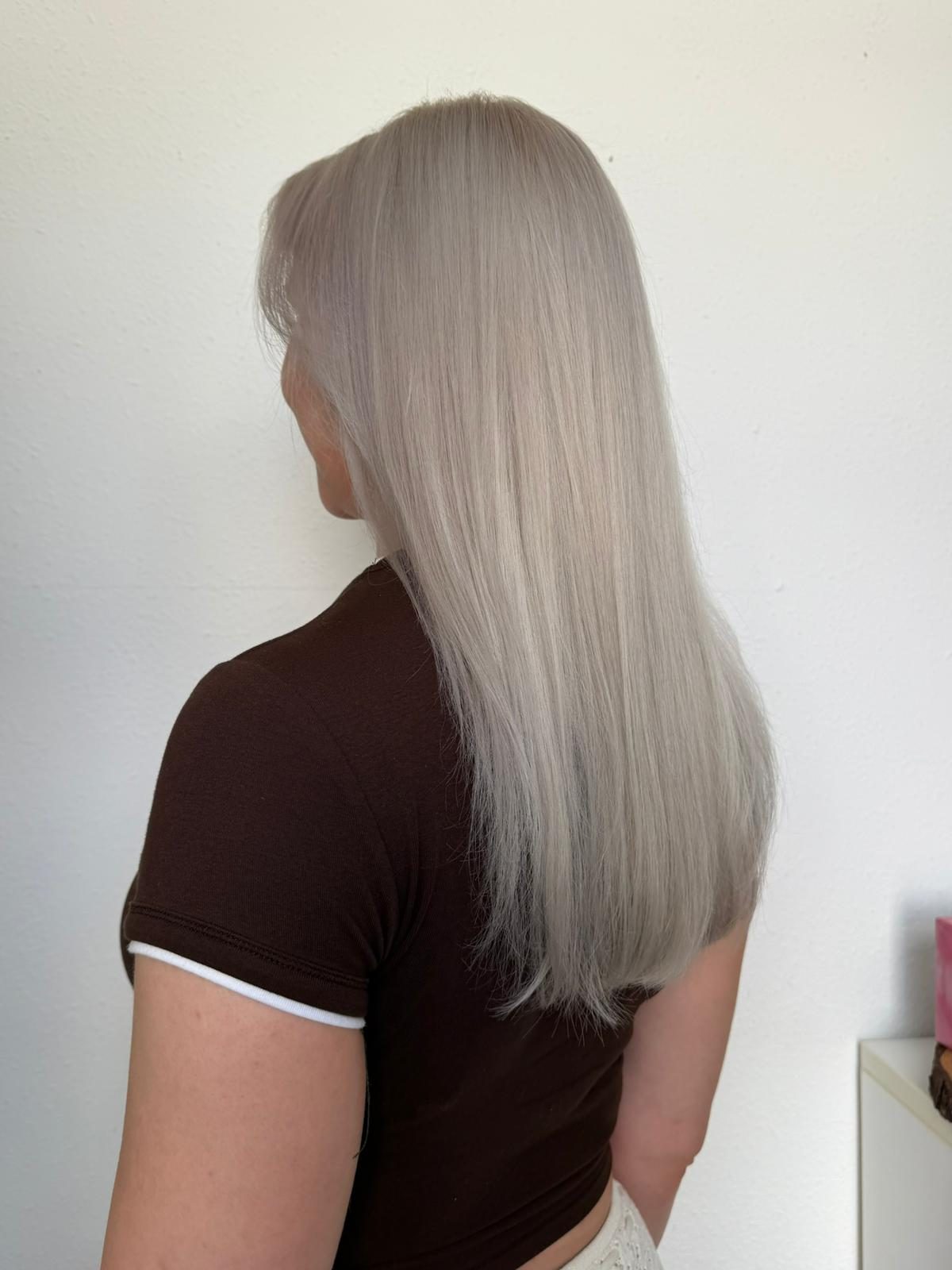 Platinblondes, glattes Haar vor hellem Hintergrund, von hinten